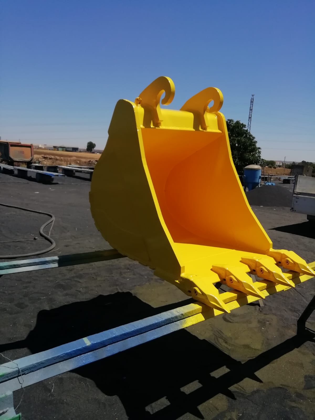Cazo de excavadora recién fabricado y pintado de amarillo, con dientes y portadientes montados
