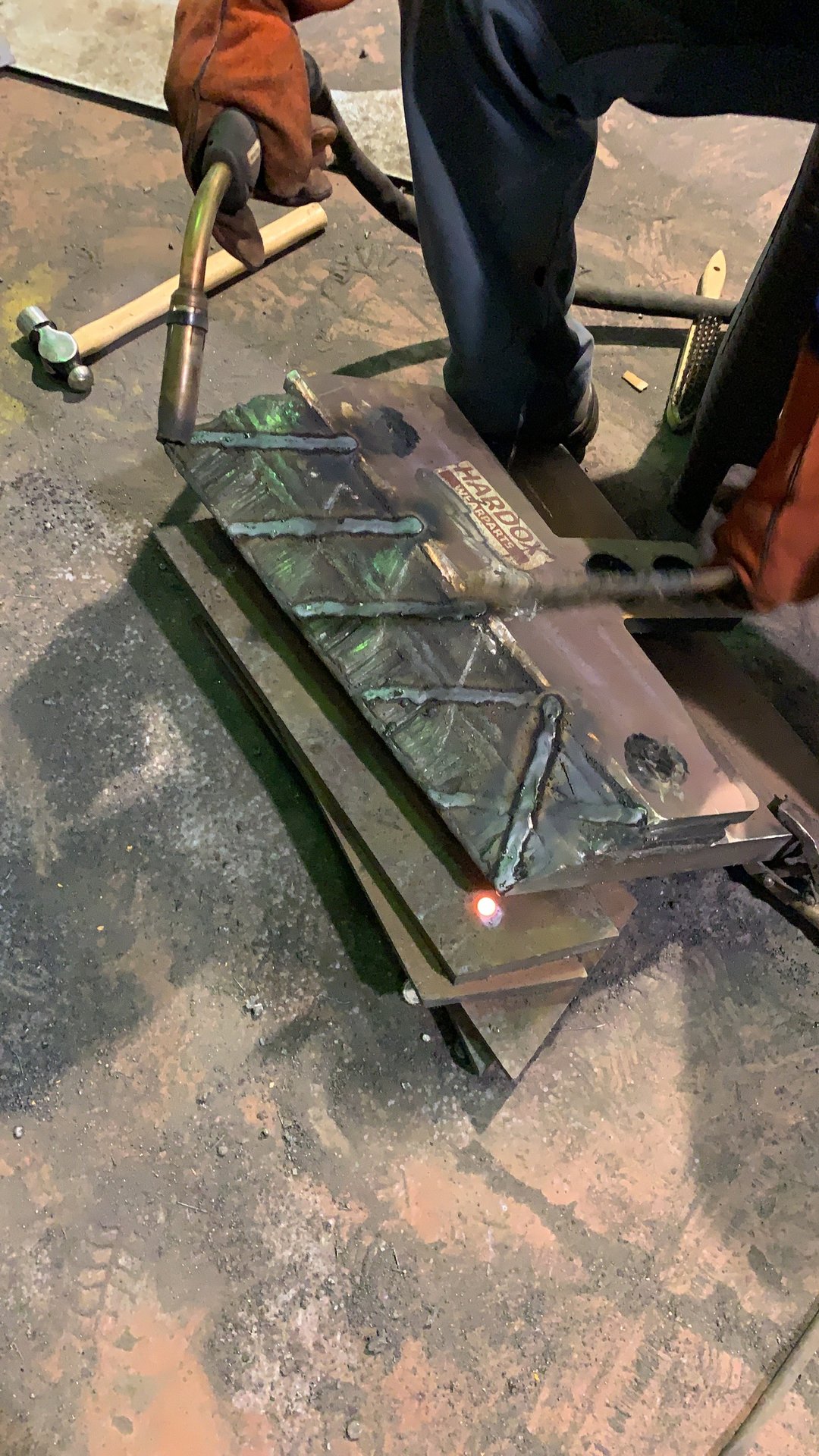 Manos aplicando recargue duro en malla romboidal, con la etiqueta Hardox Wearparts legible