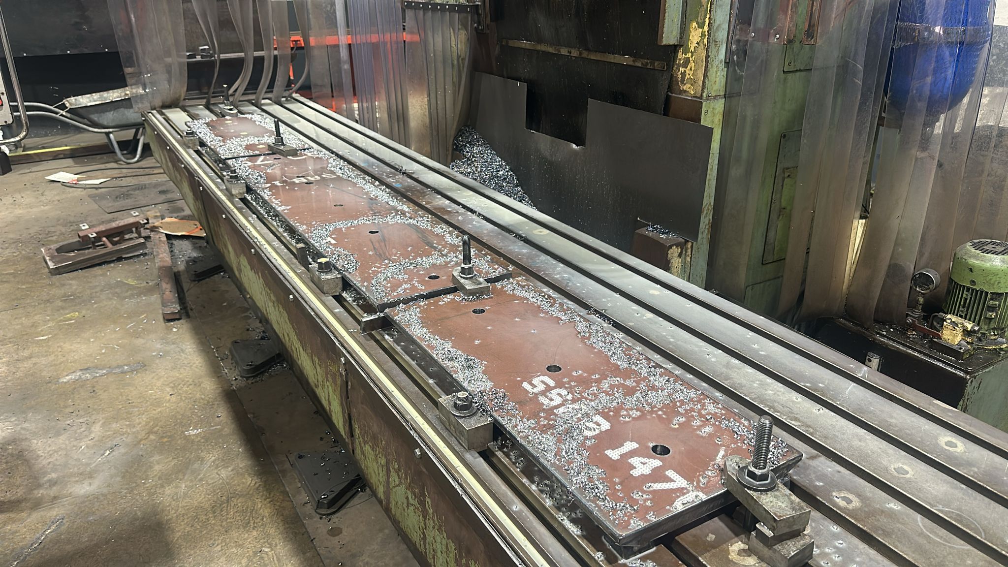 Pieza larga mecanizada, amarrada a la mesa con bridas, cubierta de viruta de acero