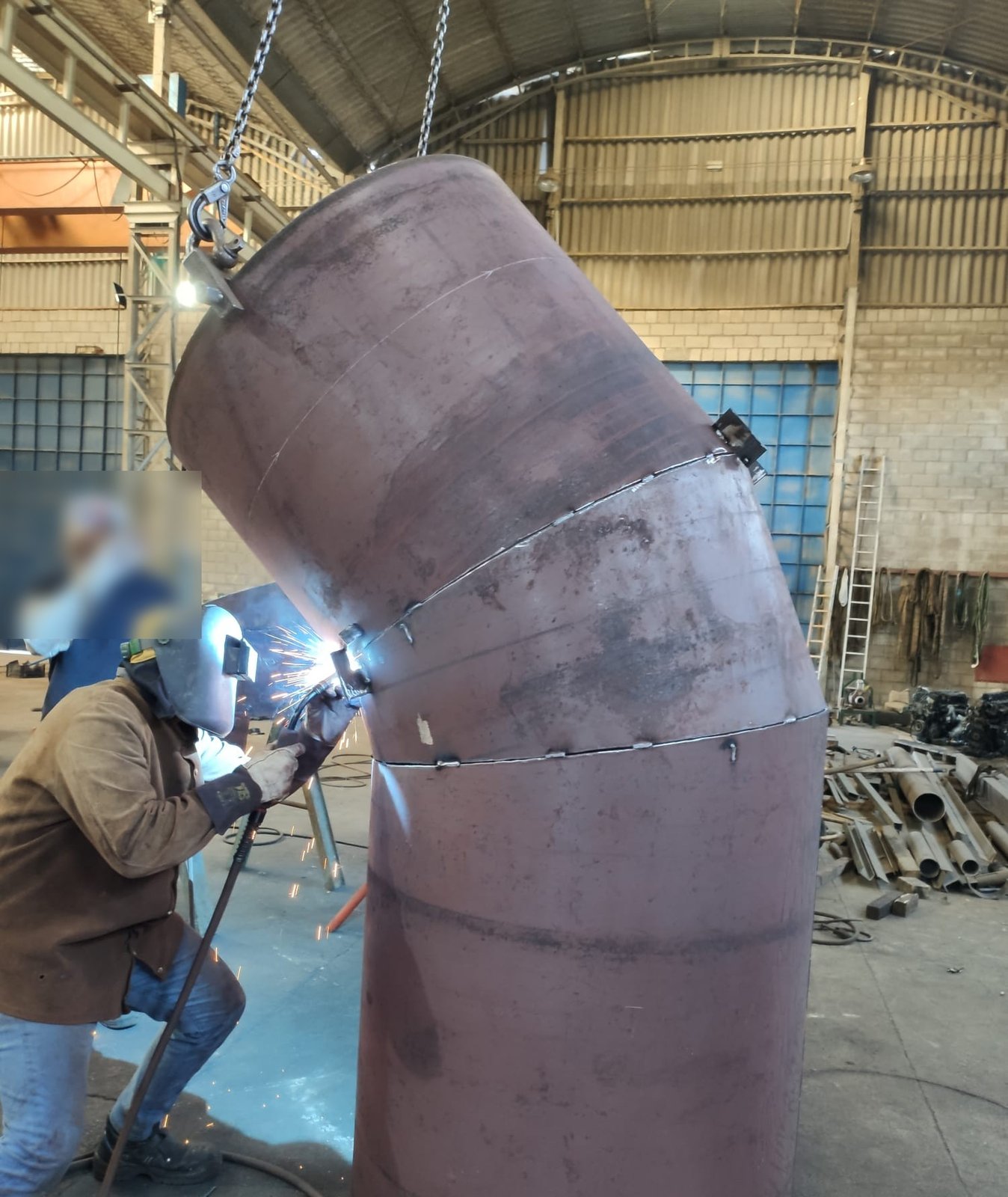 Soldador con el arco encendido sobre un tramo de spool de tubería, suspendido de la grúa